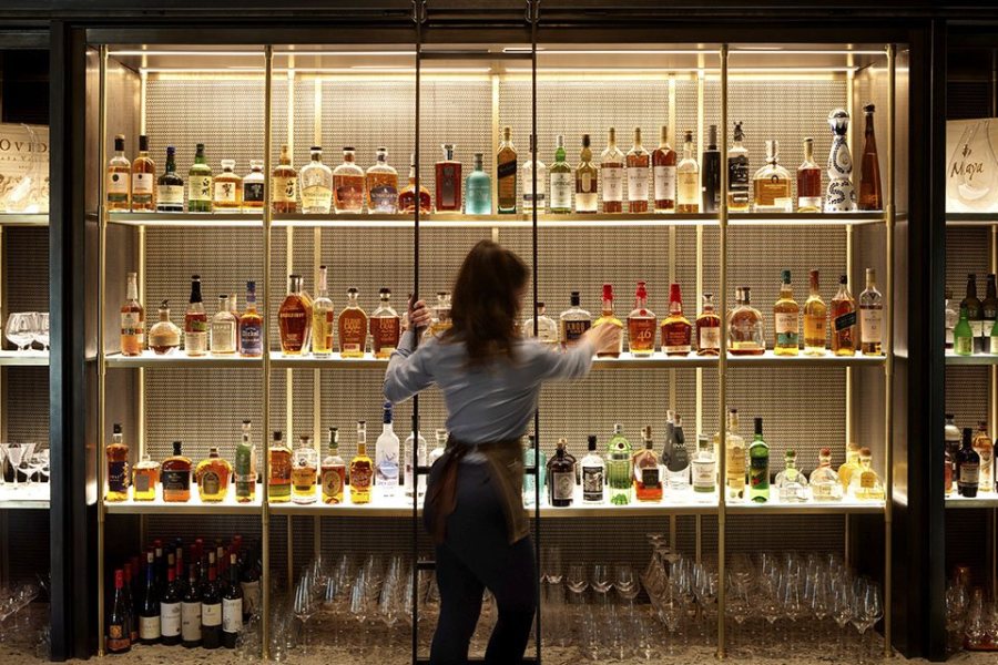 Bar tender on ladder in front of liquor bottles